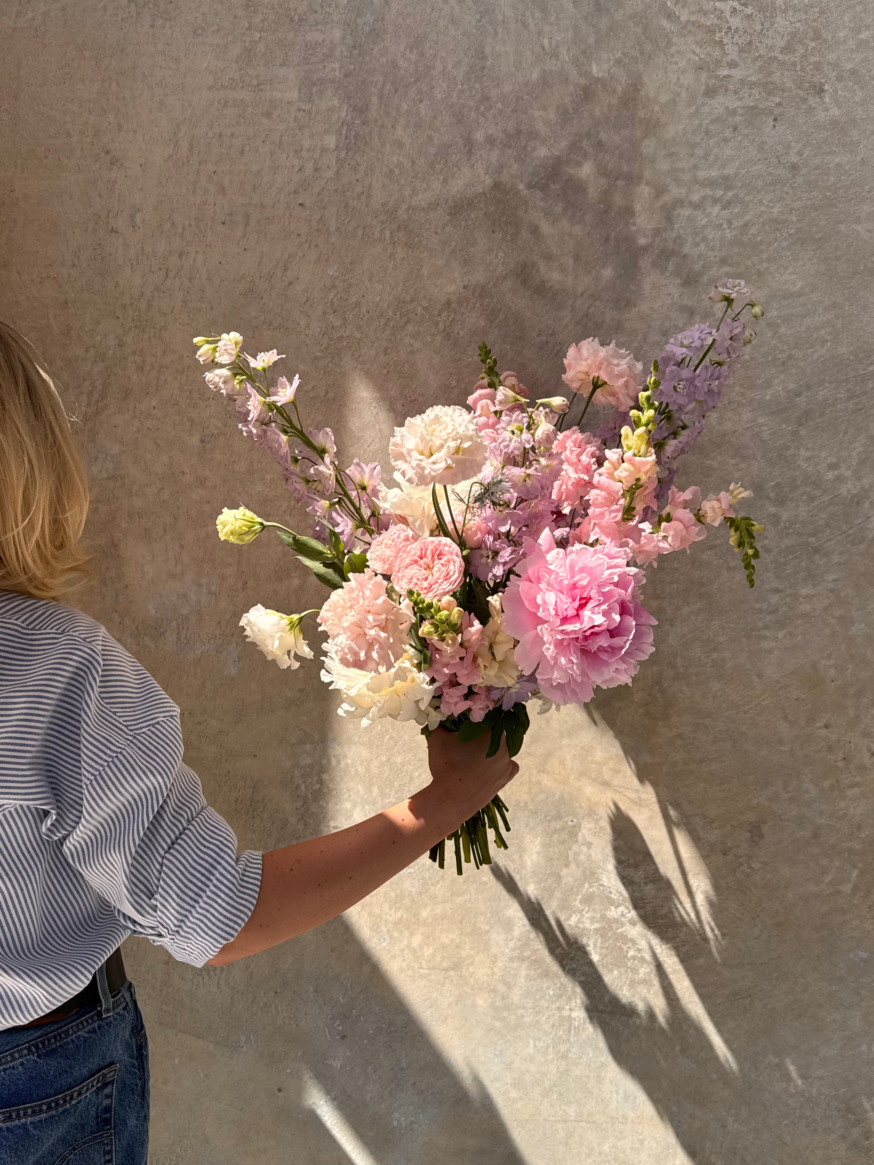 Person holding a bouquet of pink and white flowers against a textured wall.