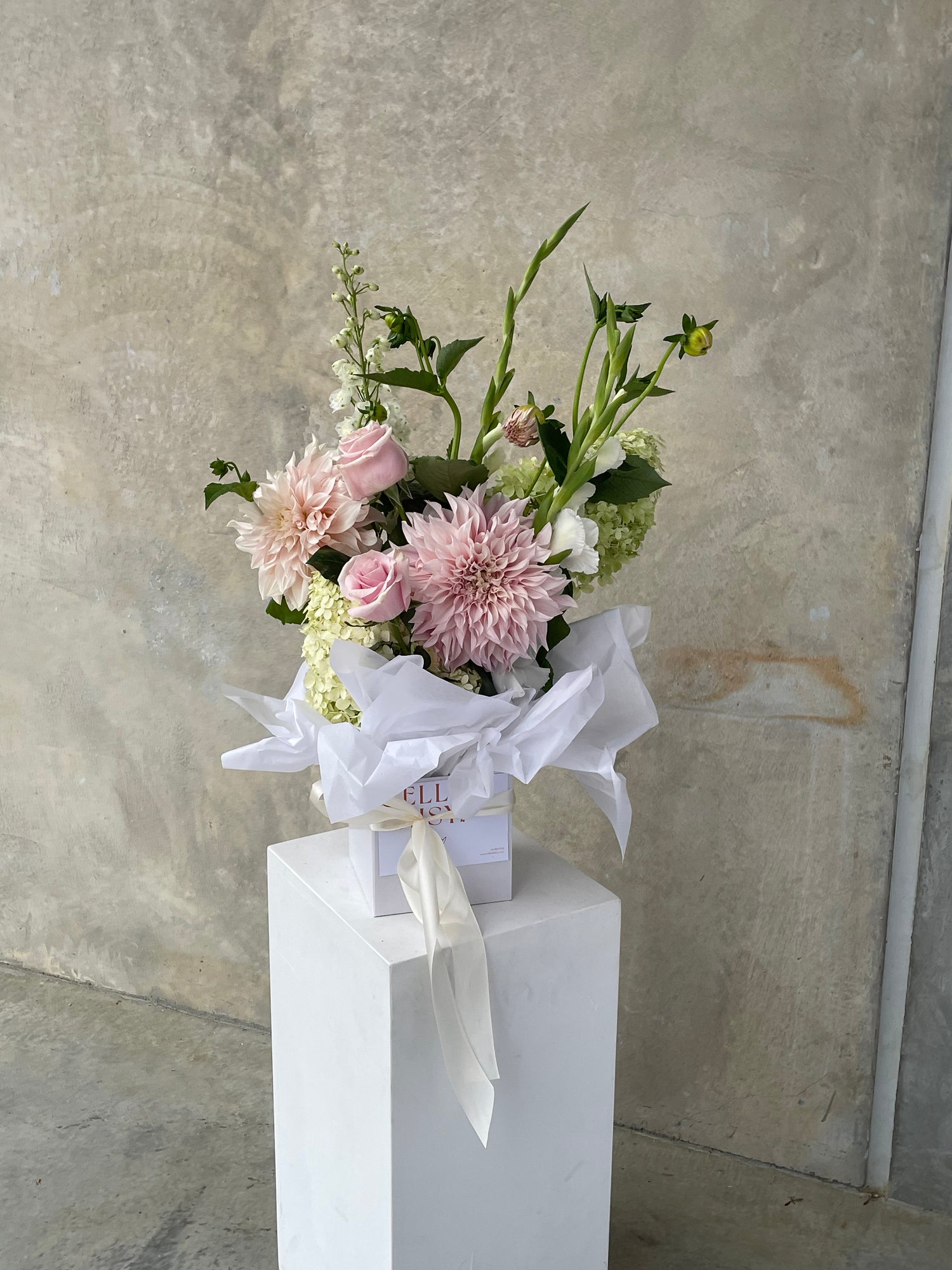 Bouquet of pink and green flowers on a white pedestal against a gray stone wall.