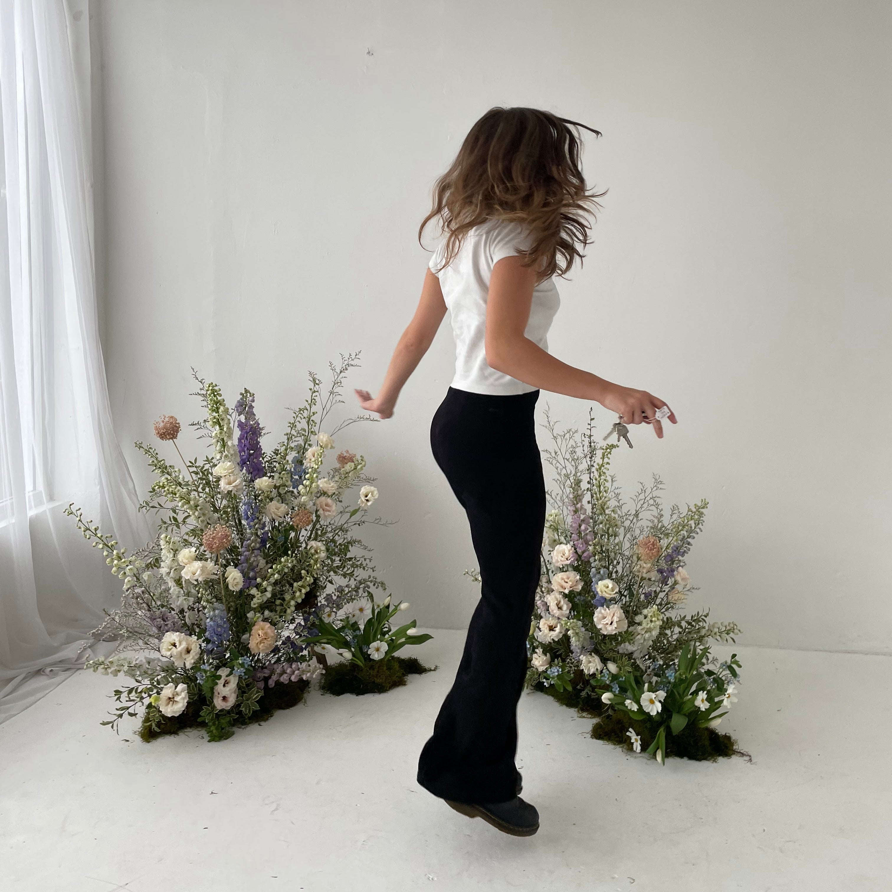 Person standing between two floral arrangements in a white room.