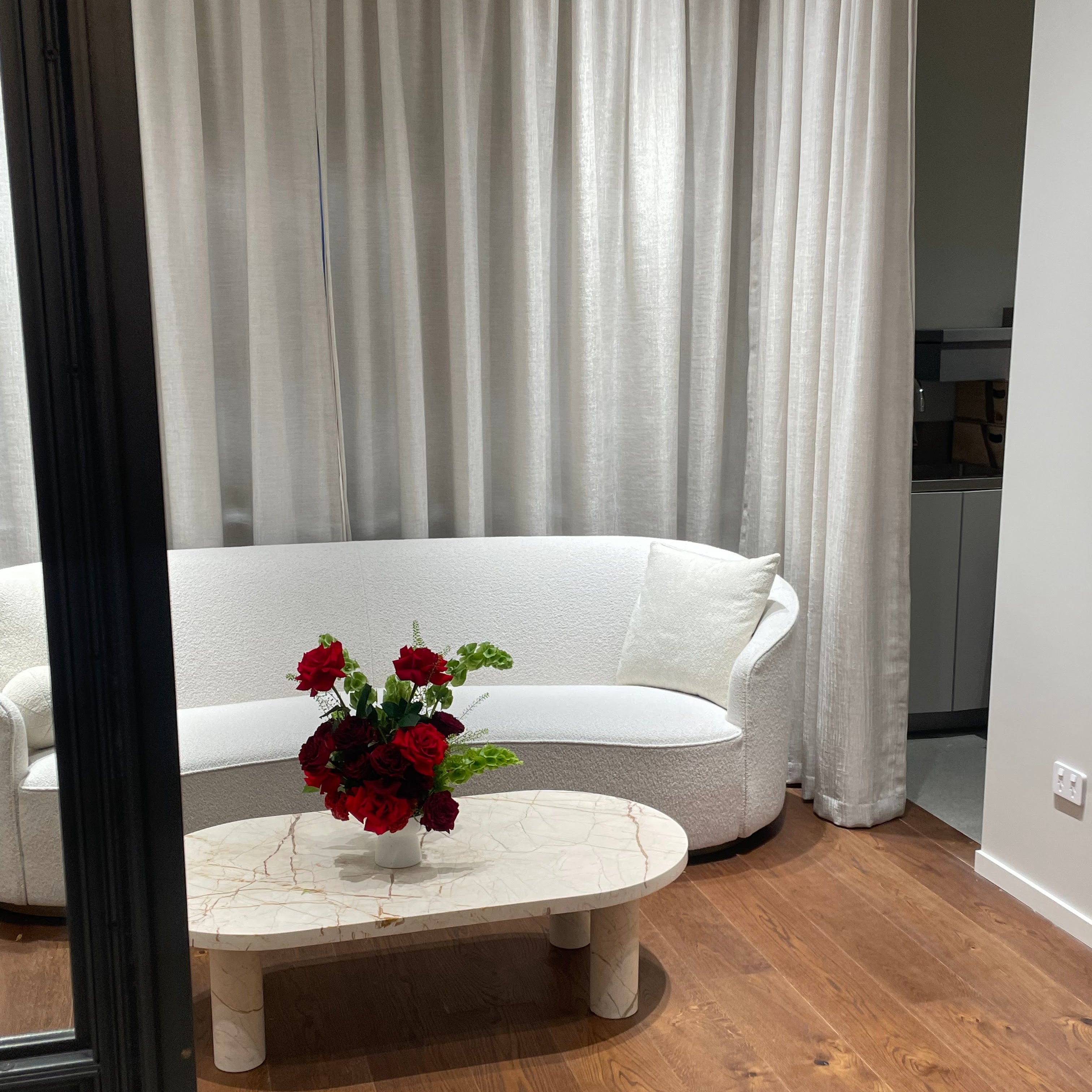 Modern living room with a white sofa, marble coffee table, and red flowers.