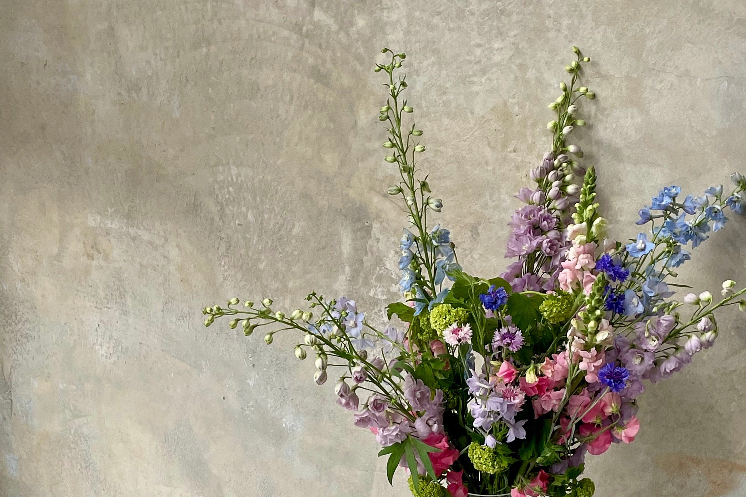 Bouquet of flowers in a glass vase on a white pedestal against a textured beige wall.