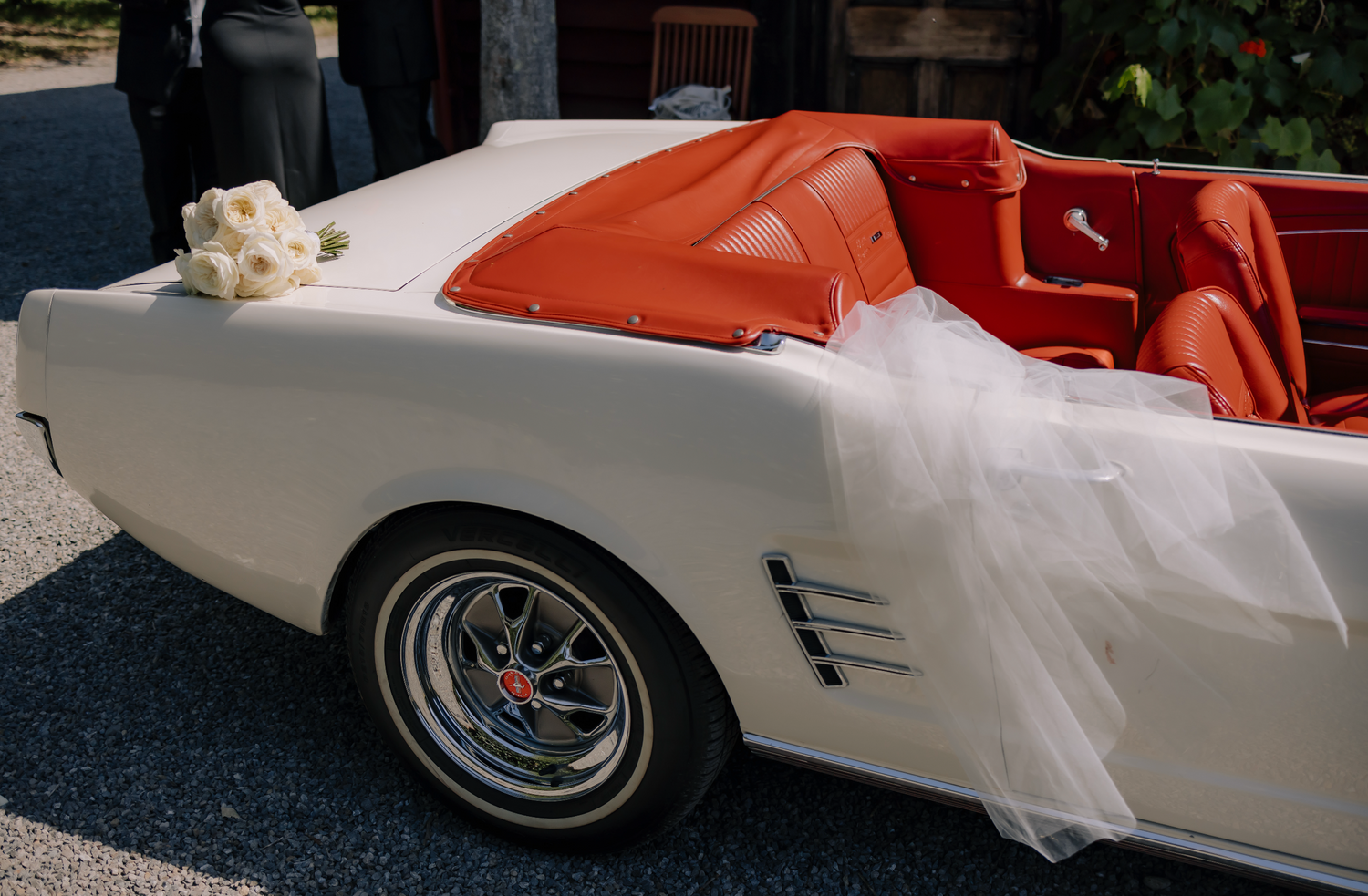 White convertible car with orange interior and a white flower arrangement on the hood, parked outdoors.