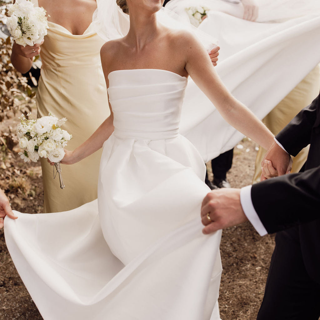 Bride in a white dress being carried by a man with a group of people in the background.